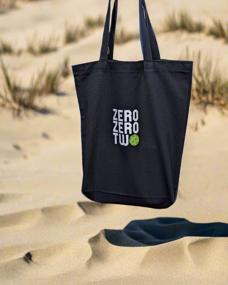 Black tote bag with 'ZERO TWO' branding held by a person on a deck.