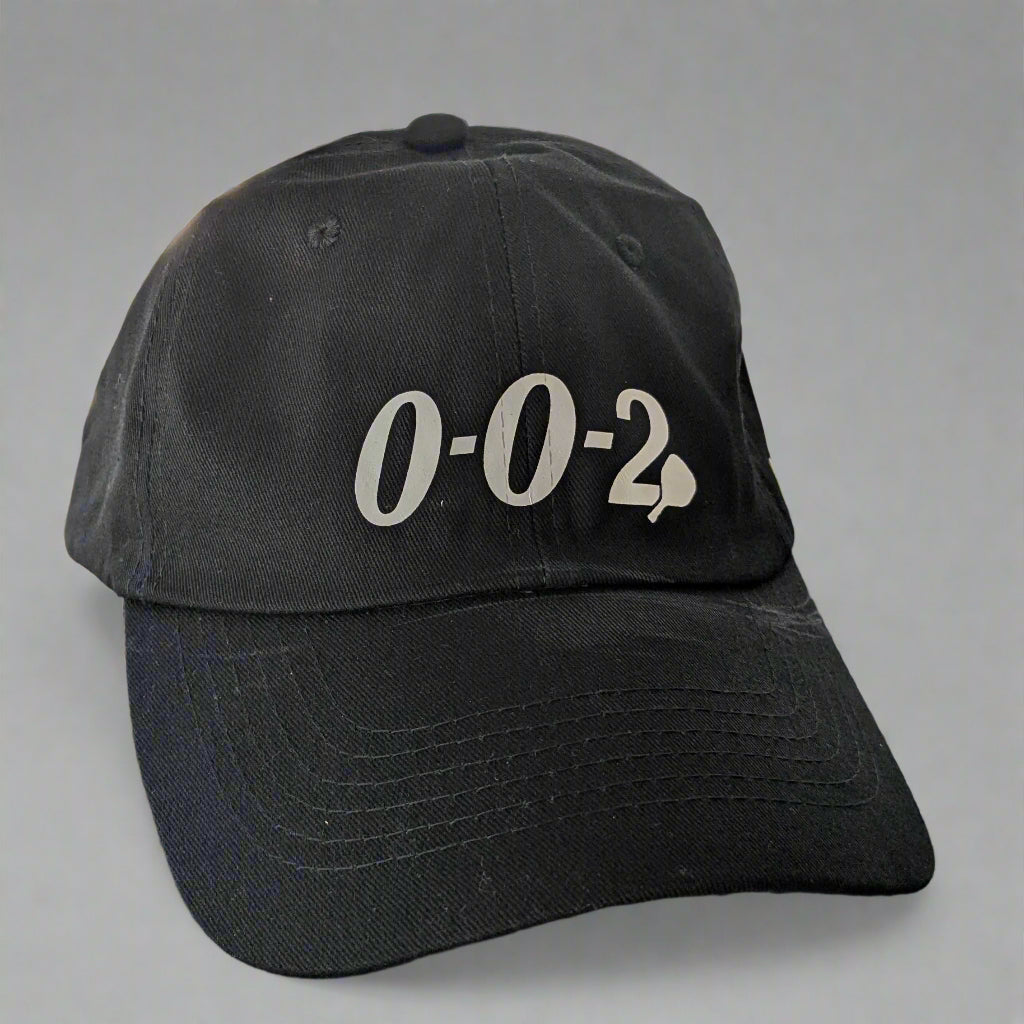 Black cap with '0-0-2' printed on it, placed on a surface with a geometric pattern.