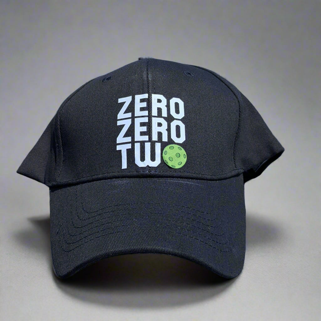 Black cap with 'ZERO ZERO TWO' text on a car hood with a store and cars in the background